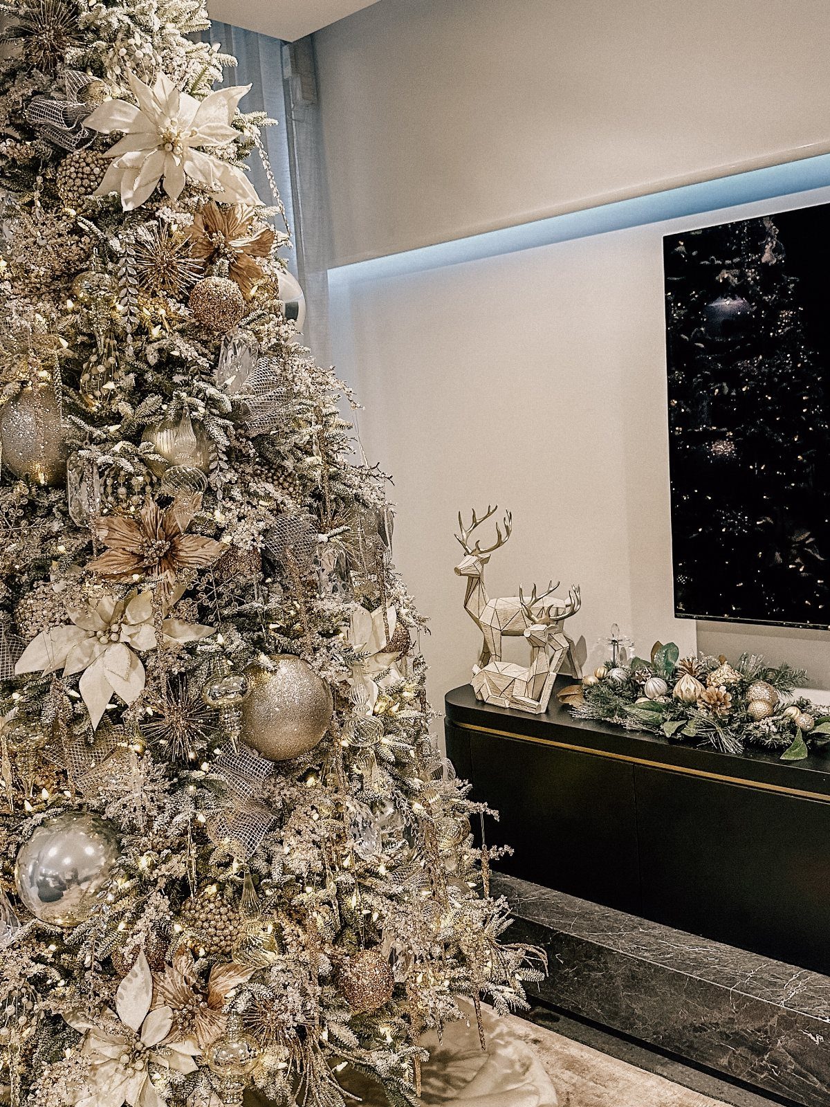 Decorated Christmas tree with gold and silver ornaments and white poinsettias in a room.