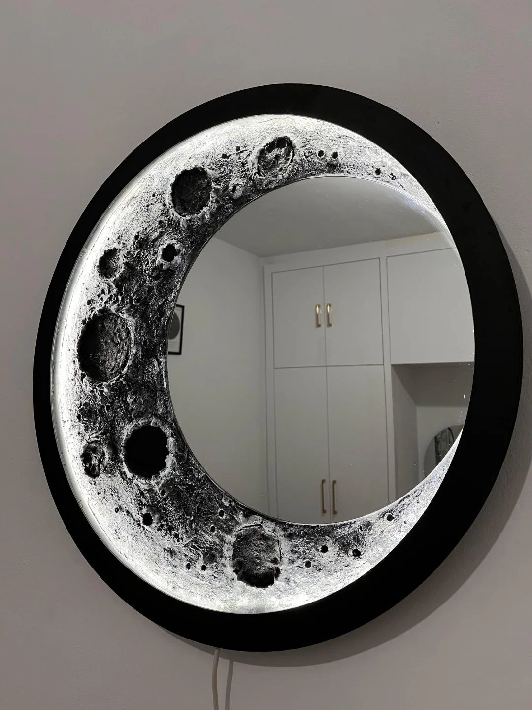 23 Cool House Items for Walls, Shelves, Desks, and Baths 3 Round moon-themed accent mirror with a glowing lunar crescent and black frame.