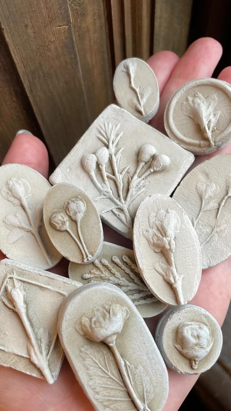 30 DIY Clay Crafts to Make with Air-Dry Clay for Home Decor 29 Small off-white clay pieces with detailed botanical imprints held in a person's hand.
