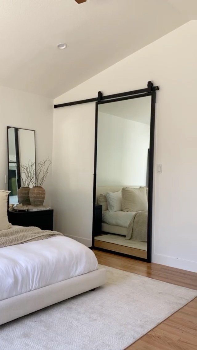 Black-framed sliding mirror door on a barn rail in a white bedroom