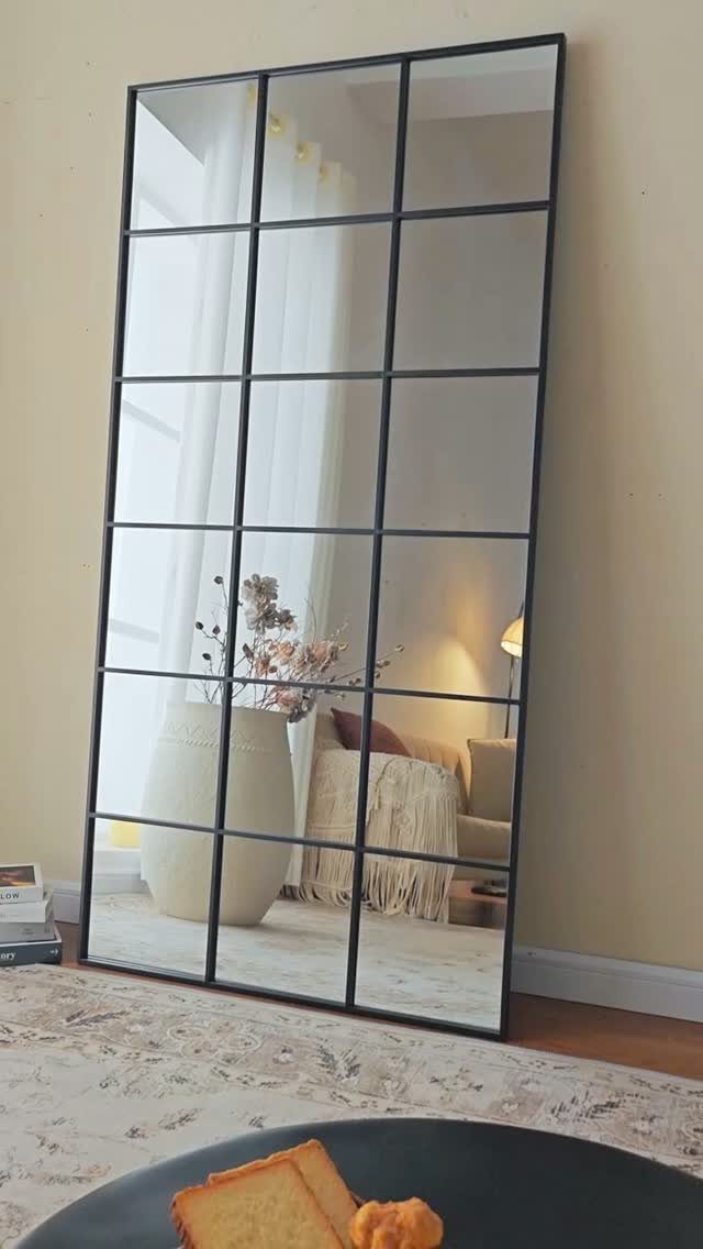 Tall black grid mirror leaning against a yellow wall in a bright living room.