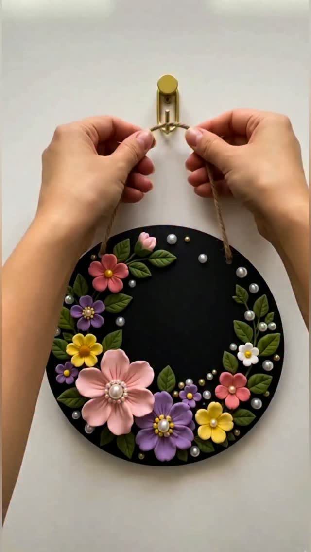30 DIY Clay Crafts to Make with Air-Dry Clay for Home Decor 8 Circular black clay wall hanging decorated with colorful 3D clay flowers and pearls.