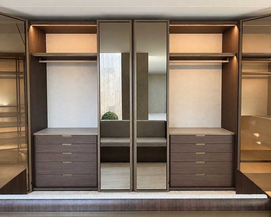Modern walk-in closet with dark wood cabinets and two tall central mirrored doors.