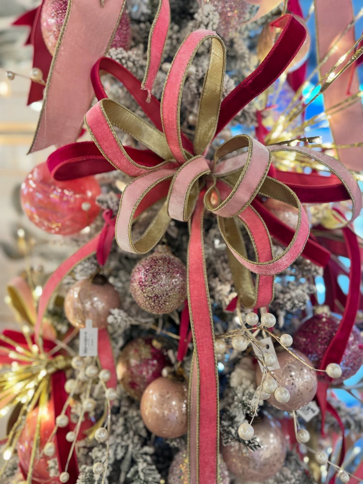 Large pink and gold velvet ribbon bows on a frosted Christmas tree with ornaments.