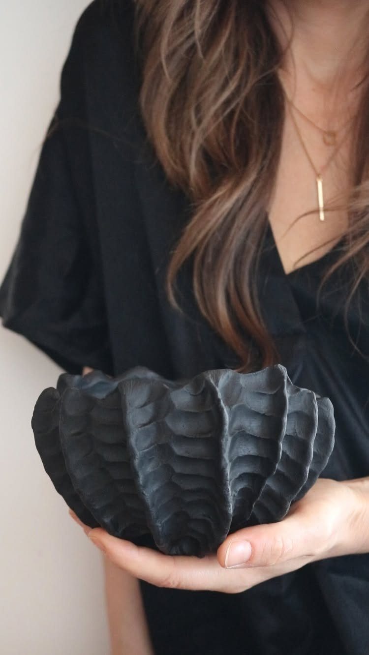 30 DIY Clay Crafts to Make with Air-Dry Clay for Home Decor 20 Hand holding a small, matte black clay bowl with a ribbed shell texture.