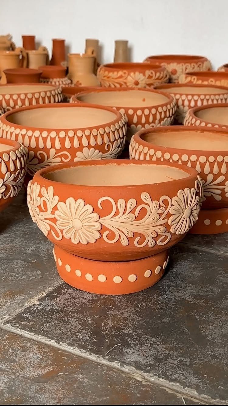 30 DIY Clay Crafts to Make with Air-Dry Clay for Home Decor 7 Terracotta clay pots with white embossed floral patterns arranged on a stone floor.