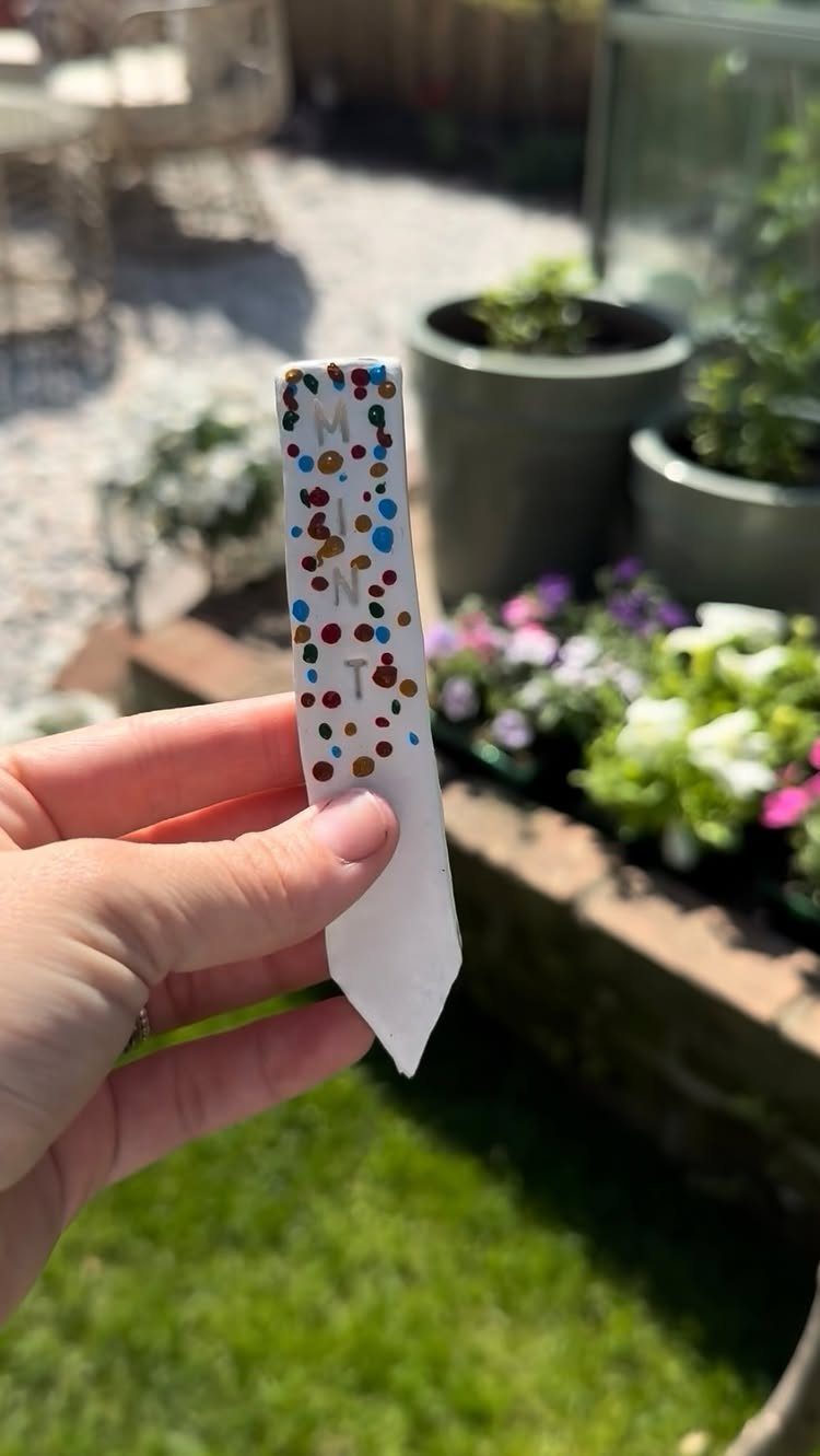 30 DIY Clay Crafts to Make with Air-Dry Clay for Home Decor 14 White clay garden marker with MINT text and colorful dots held in hand.