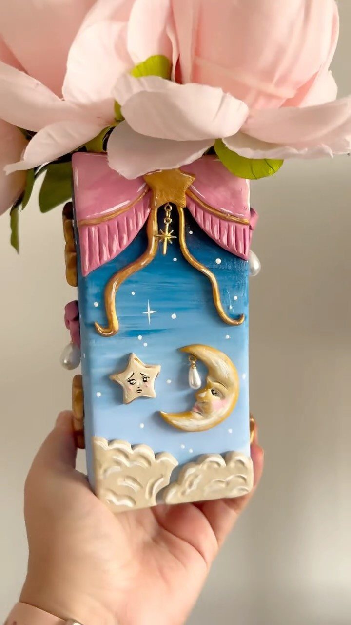 30 DIY Clay Crafts to Make with Air-Dry Clay for Home Decor 5 Small blue clay house vase with gold moon and stars holding pink flowers.