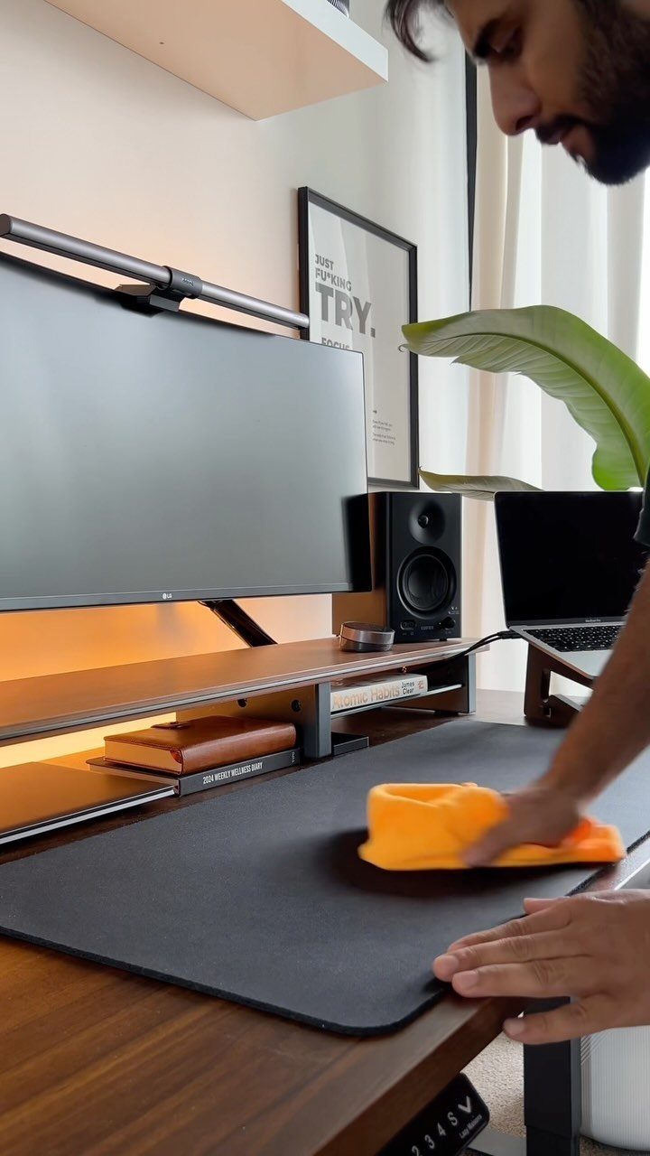 Man cleaning a black desk mat with a yellow cloth in a modern workspace.