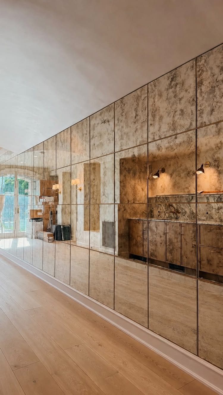 Antiqued gold mirror wall panels reflecting a room with wooden cabinets and flooring.