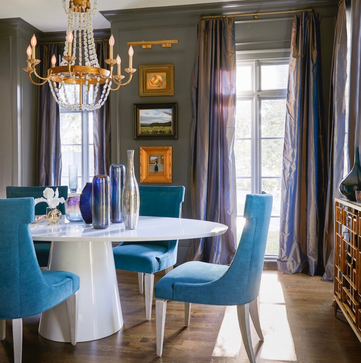 White oval dining table with teal blue chairs in a grey room