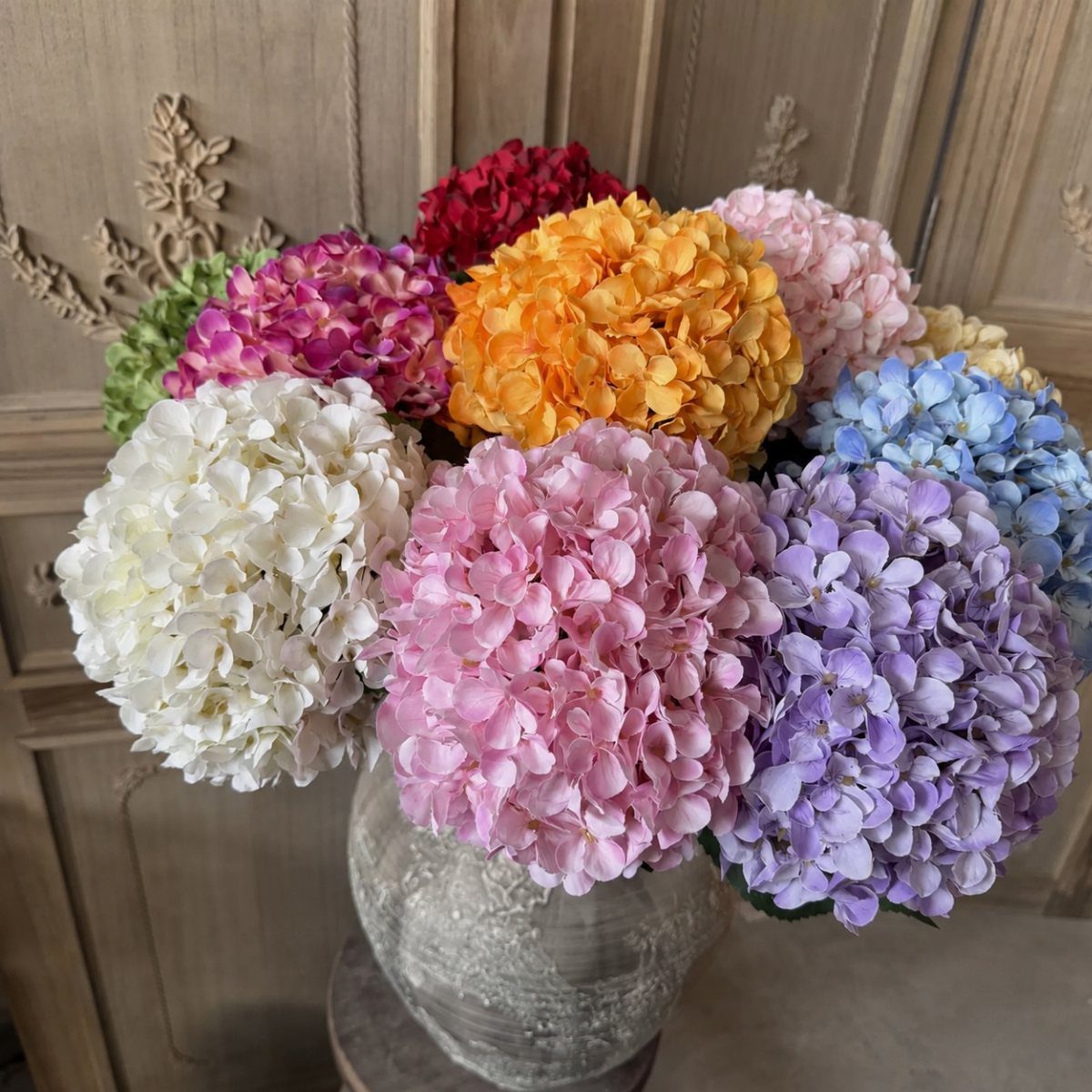 12 Artificial Flowers Decor Ideas, from Vases to Gift Boxes 4 Colorful artificial hydrangea flowers in a grey ceramic vase against a wooden background.