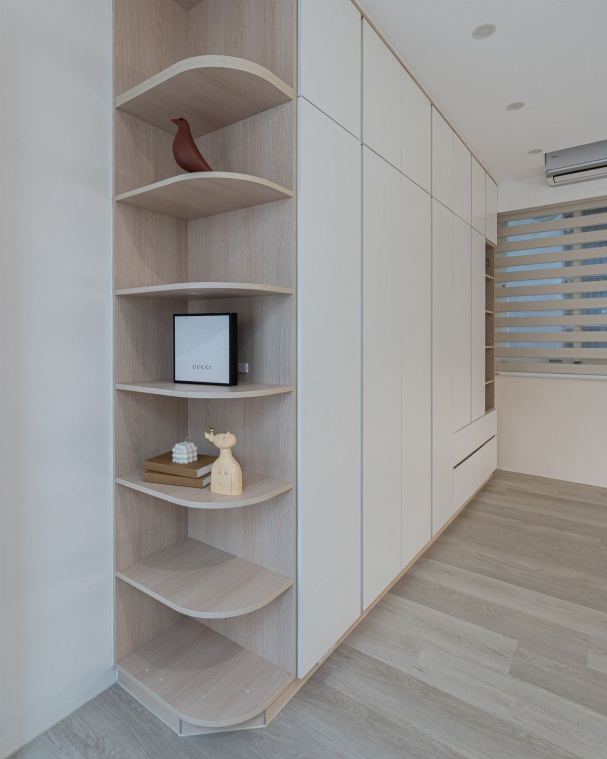 Curved light wood corner shelves integrated into a white built-in wardrobe system.