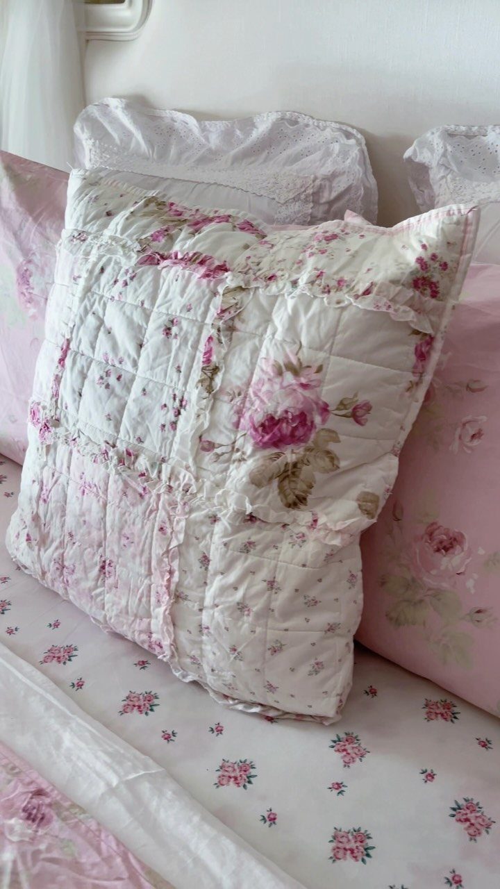 Floral rose patterned pillows and white lace bedding in a romantic bedroom setting.