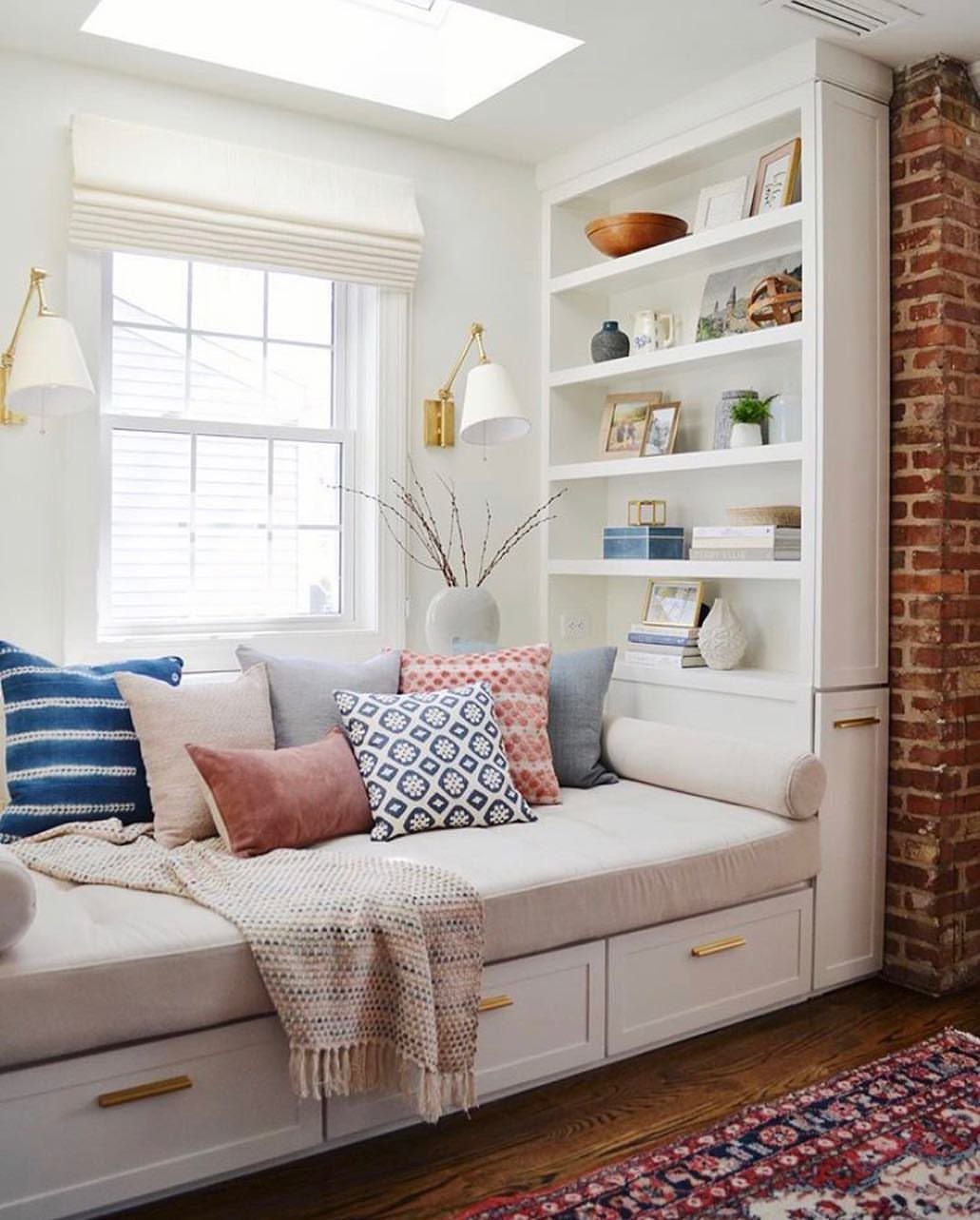 White built-in daybed reading nook with colorful pillows and adjacent white bookshelves.