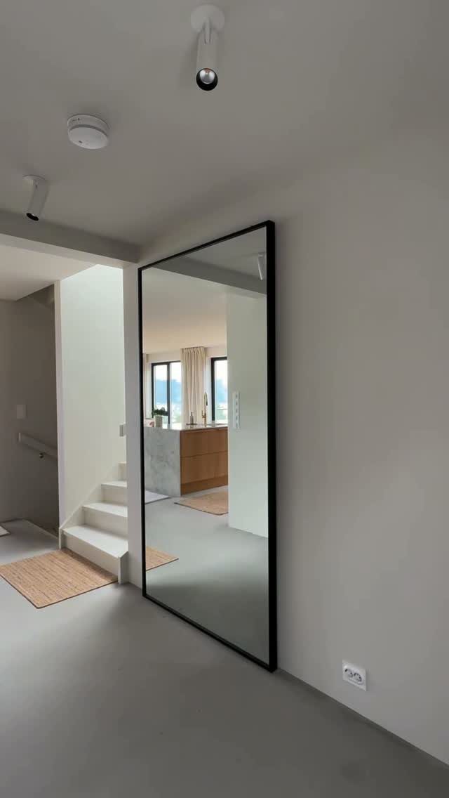 Full-length mirror with a black frame leaning against a white wall in a hallway.