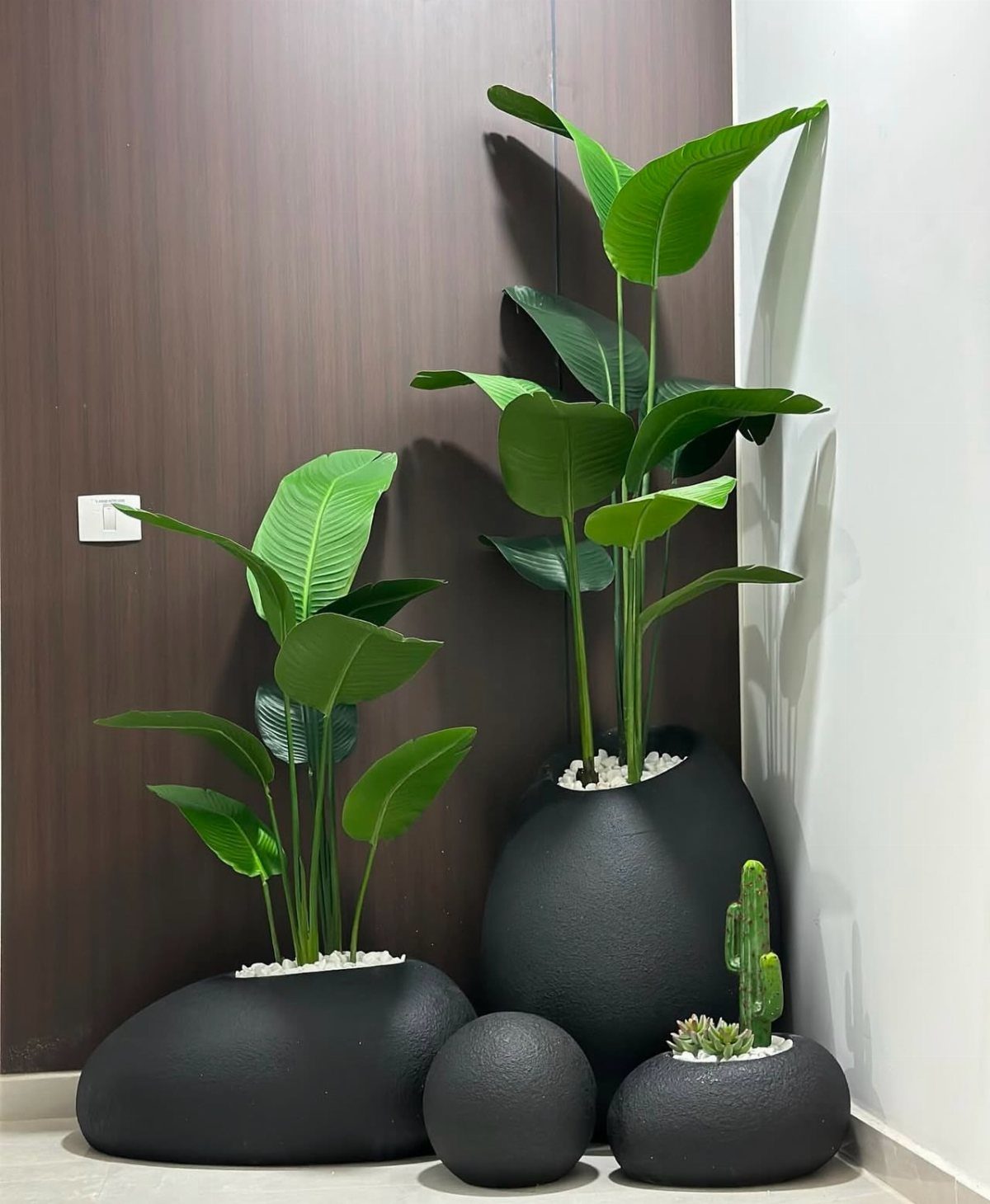 23 Cool House Items for Walls, Shelves, Desks, and Baths 2 Matte black pebble-shaped planters with green indoor plants against a neutral wall.