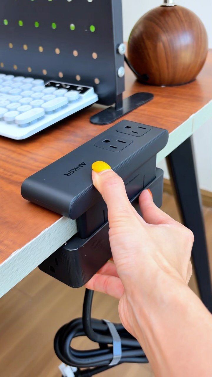 23 Cool House Items for Walls, Shelves, Desks, and Baths 18 Black Anker power strip clamped to a wooden desk with a hand holding it.