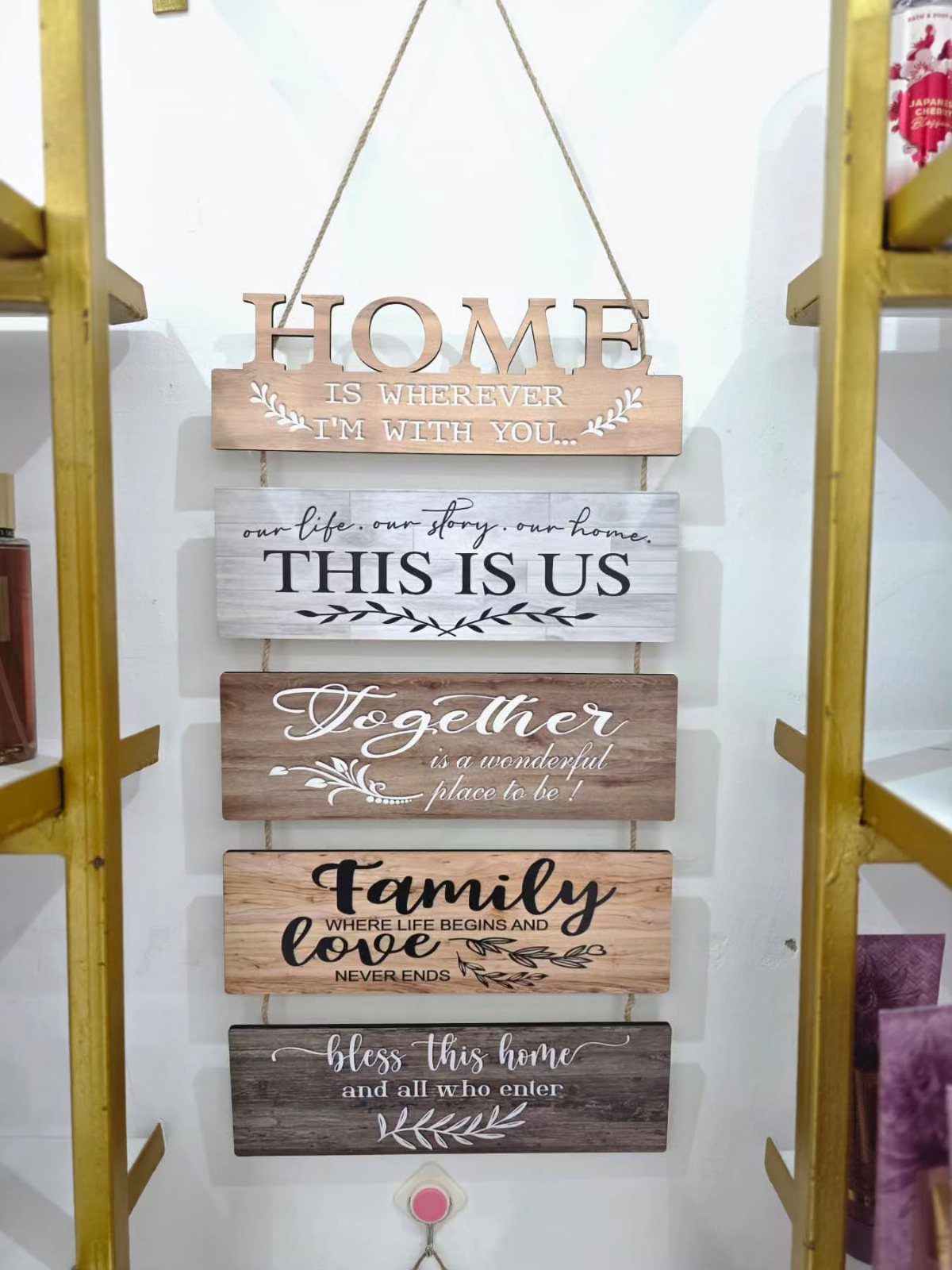 Wooden signs with family quotes hanging vertically on a white wall between gold shelves.