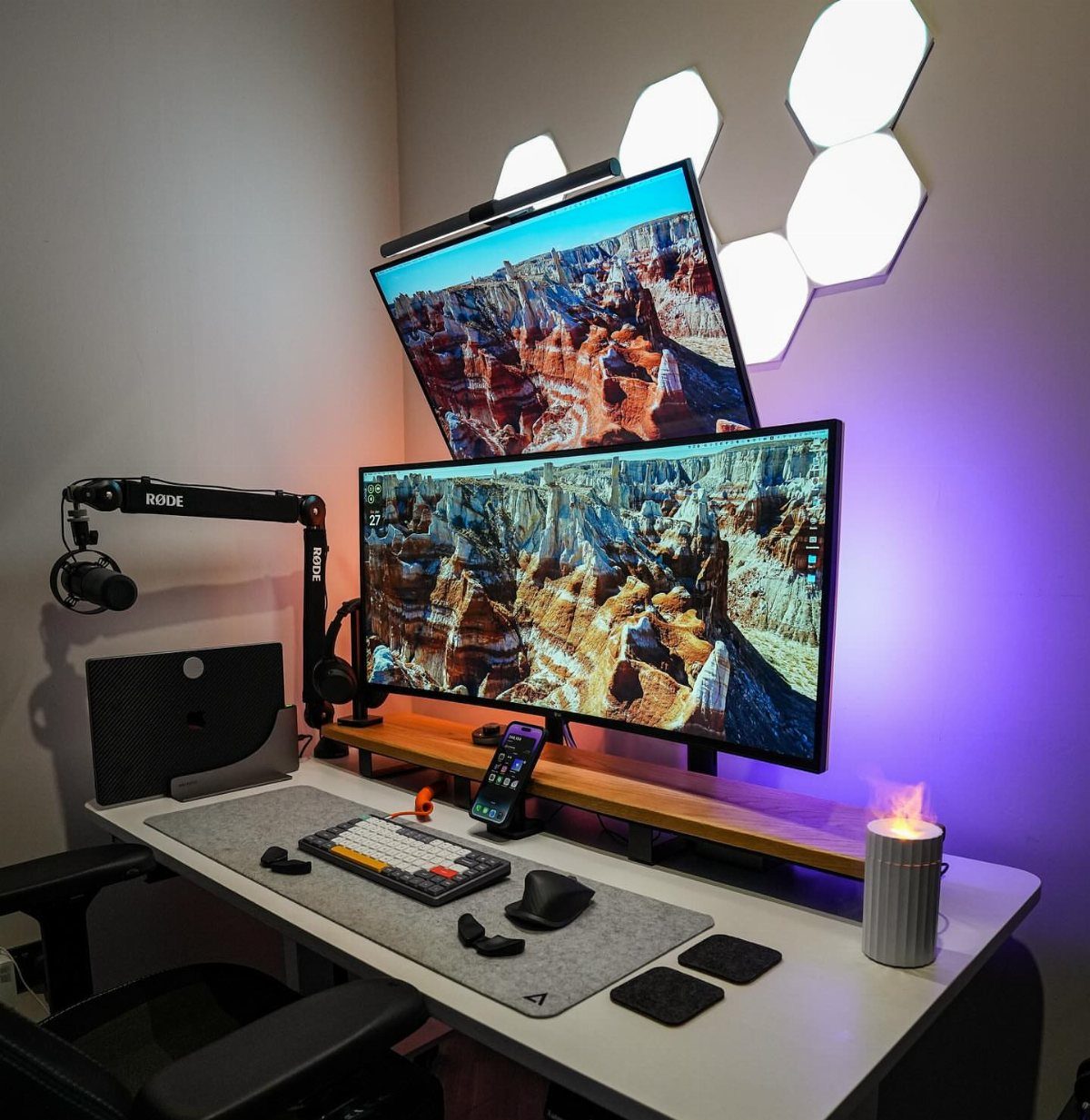 Dual monitor desk setup with stacked screens, gaming peripherals, and hexagonal wall lighting.