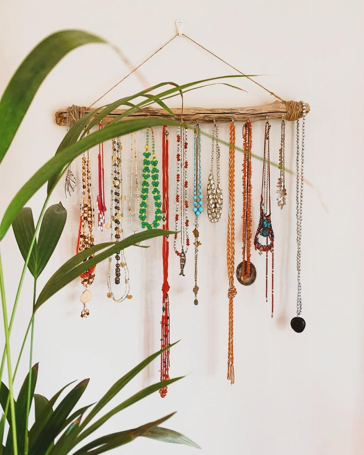 Driftwood jewelry hanger holding various colorful beaded necklaces against a white wall.