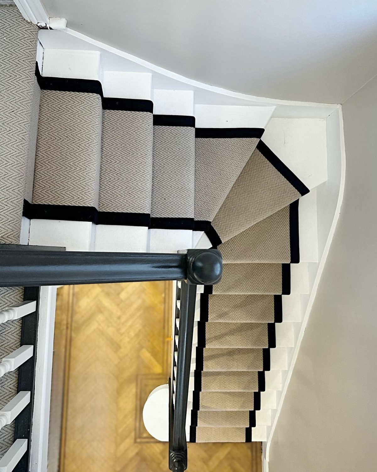 Stairs with Carpet: 23 Styles from Runners to Bold Patterns 14 Beige textured carpet runner with black borders on white stairs above herringbone wood flooring.