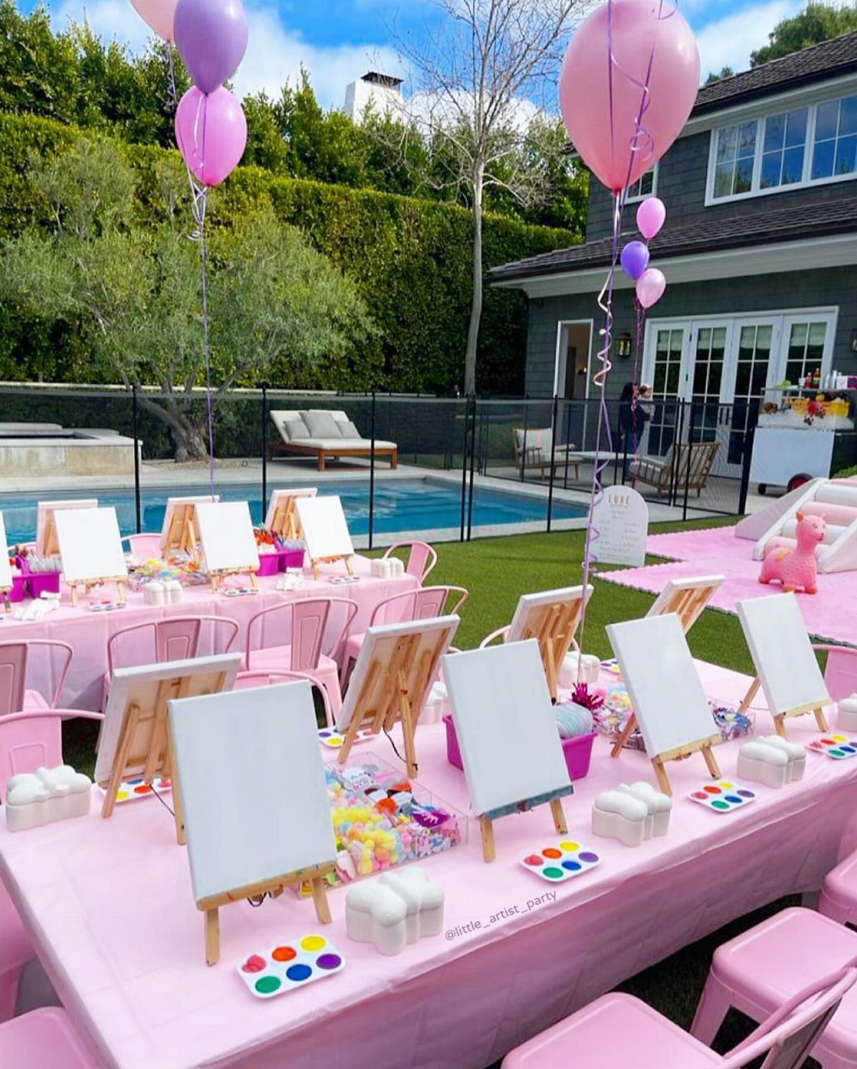 Small wooden easels with white canvases on pink tables at an outdoor party.