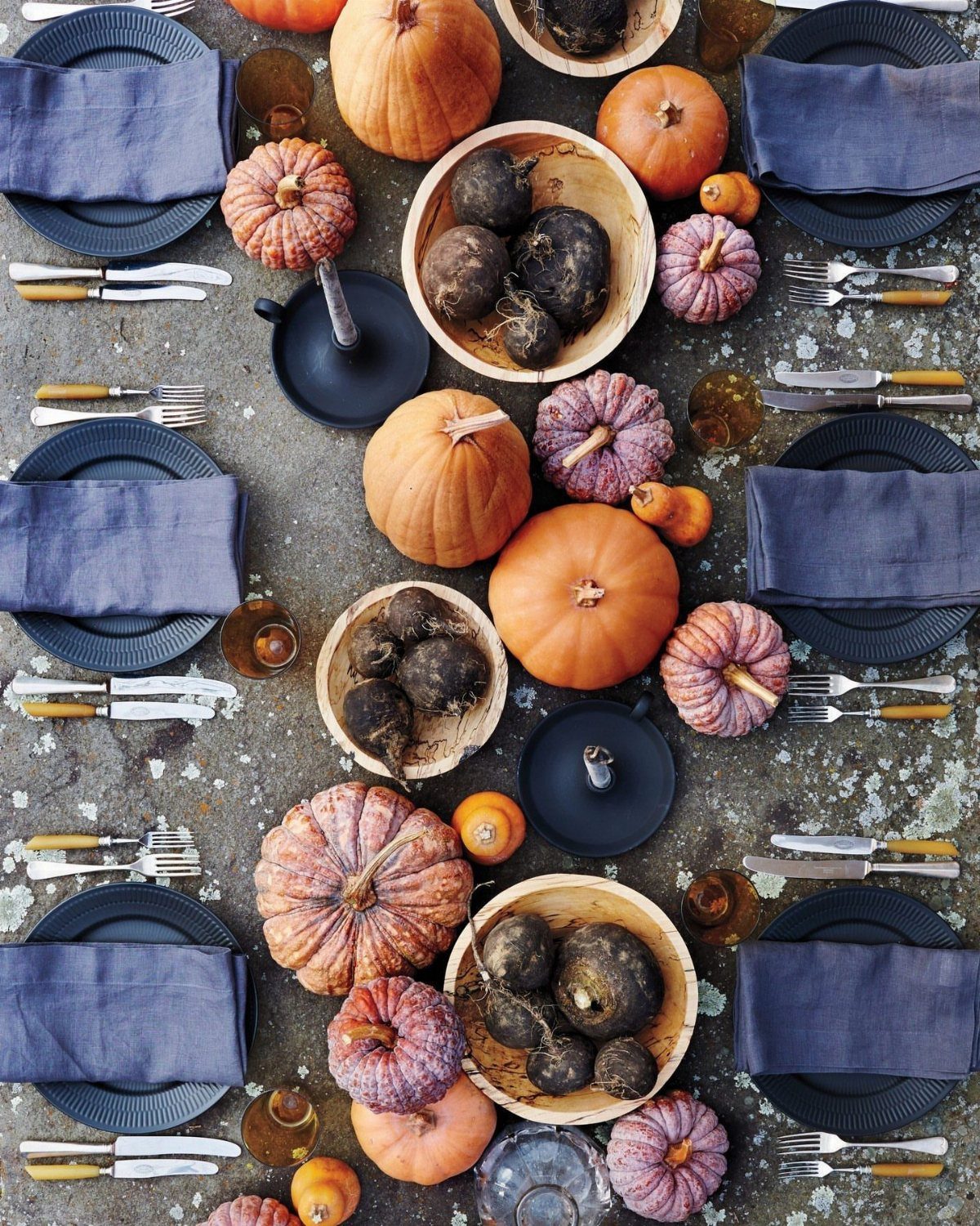 Orange and purple pumpkins with navy blue plates and napkins on a stone table.