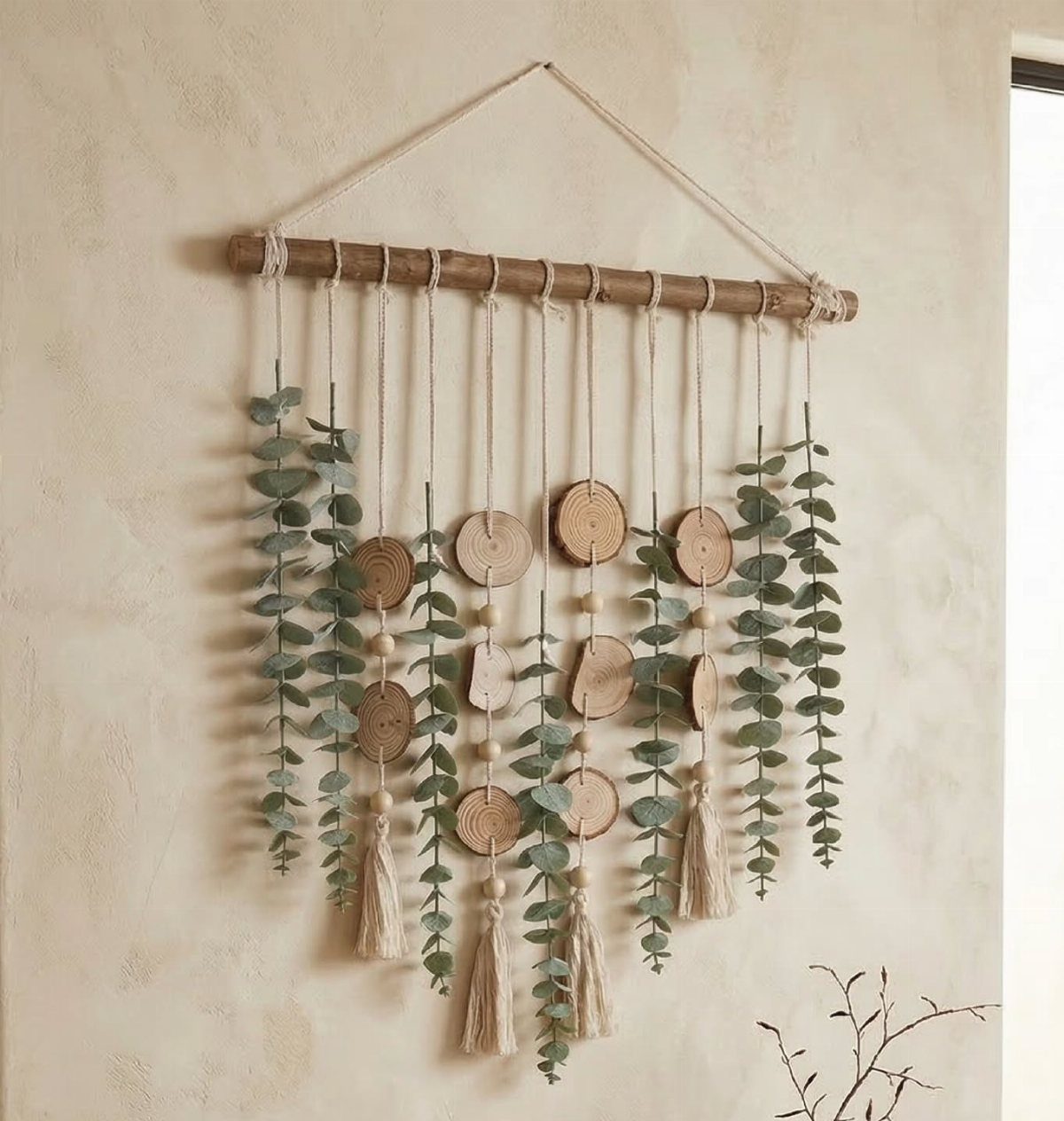 Wall hanging with felt eucalyptus leaves, wooden slices, and tassels on a wooden branch.