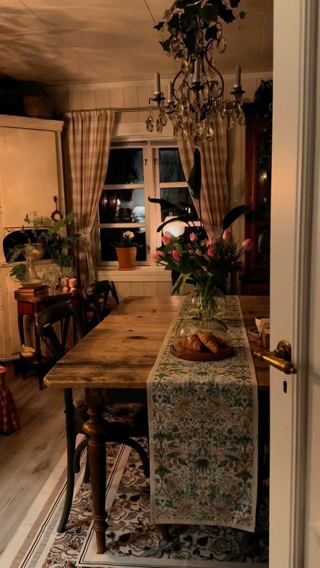 Rustic dining room with a wooden table, floral runner, and crystal chandelier.