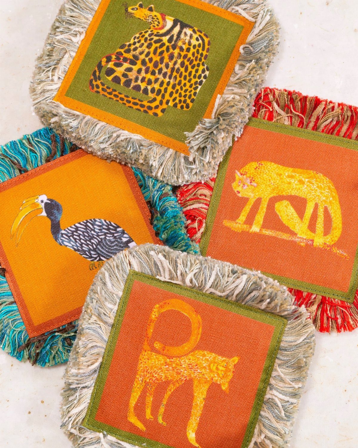 23 Cool House Items for Walls, Shelves, Desks, and Baths 9 Fringed fabric coasters with colorful animal illustrations on a light surface.