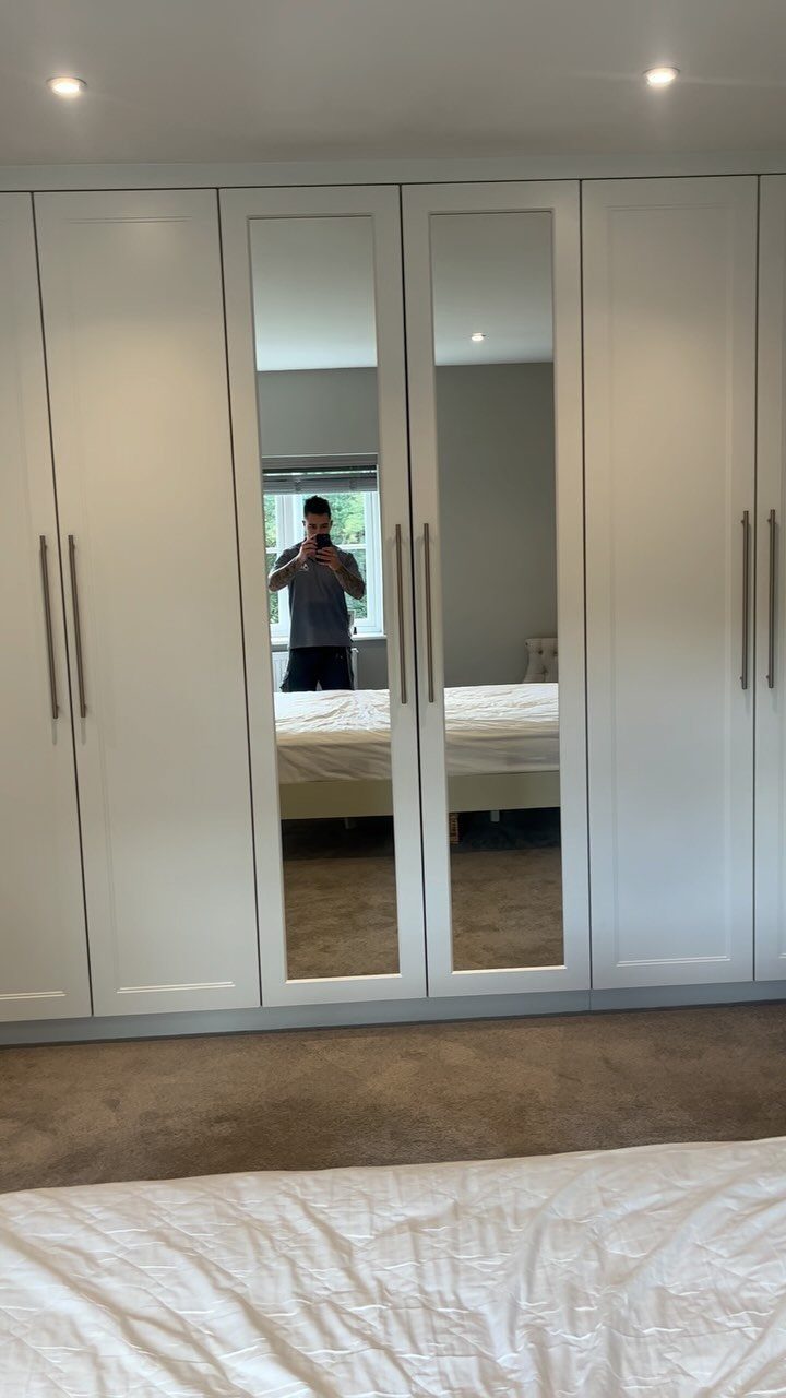 White built-in wardrobe with two central full-length mirrored doors in a bedroom.