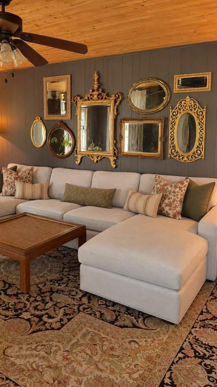 Collection of gold-framed mirrors on a grey wall above a white sectional sofa.