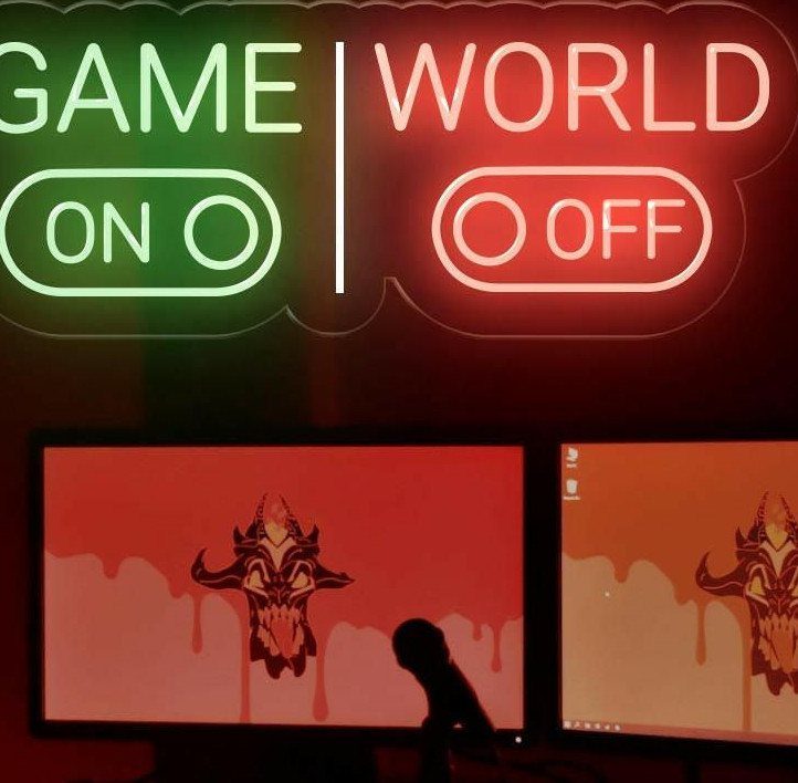 Neon sign reading Game On World Off above two computer monitors in a room.