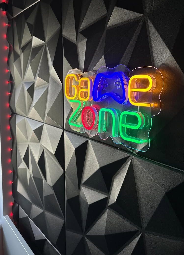 Game Zone neon sign with a blue controller on a black geometric wall