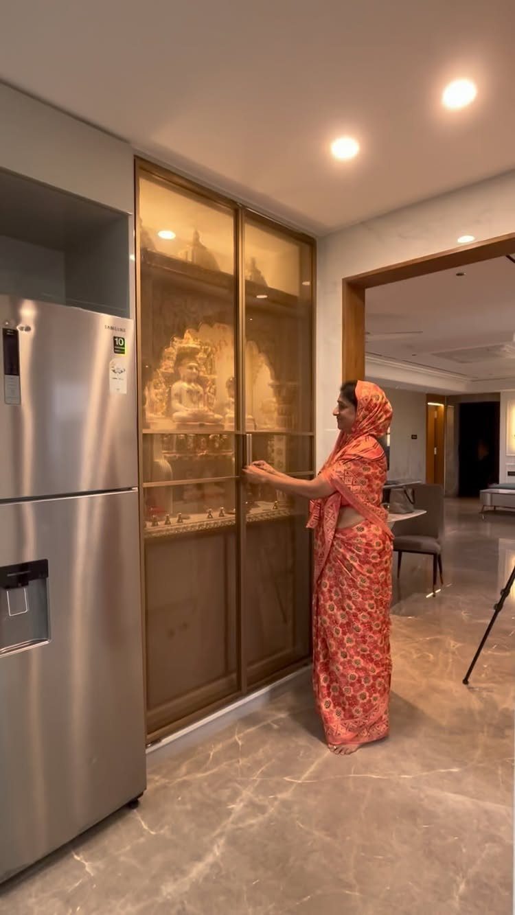34 Puja Unit Design Modern Ideas for Your Home in 2026 4 Woman in red saree standing by a gold-framed glass-door puja unit with idols.