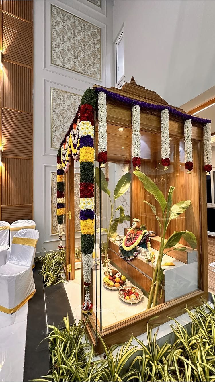 34 Puja Unit Design Modern Ideas for Your Home in 2026 3 Glass enclosed wooden puja mandir decorated with colorful floral garlands and indoor plants