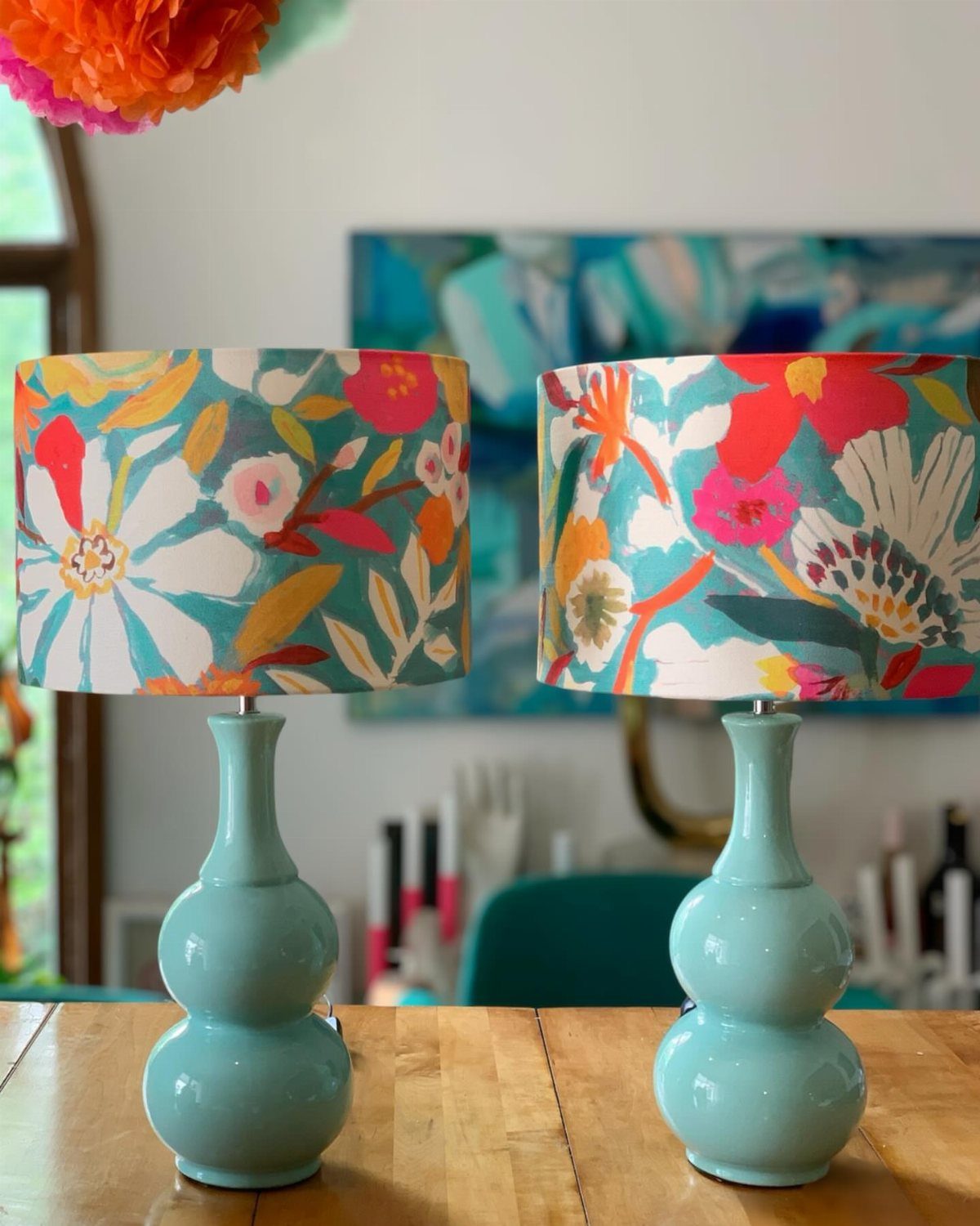 Two turquoise ceramic lamps with colorful hand painted floral lamp shades on a table.