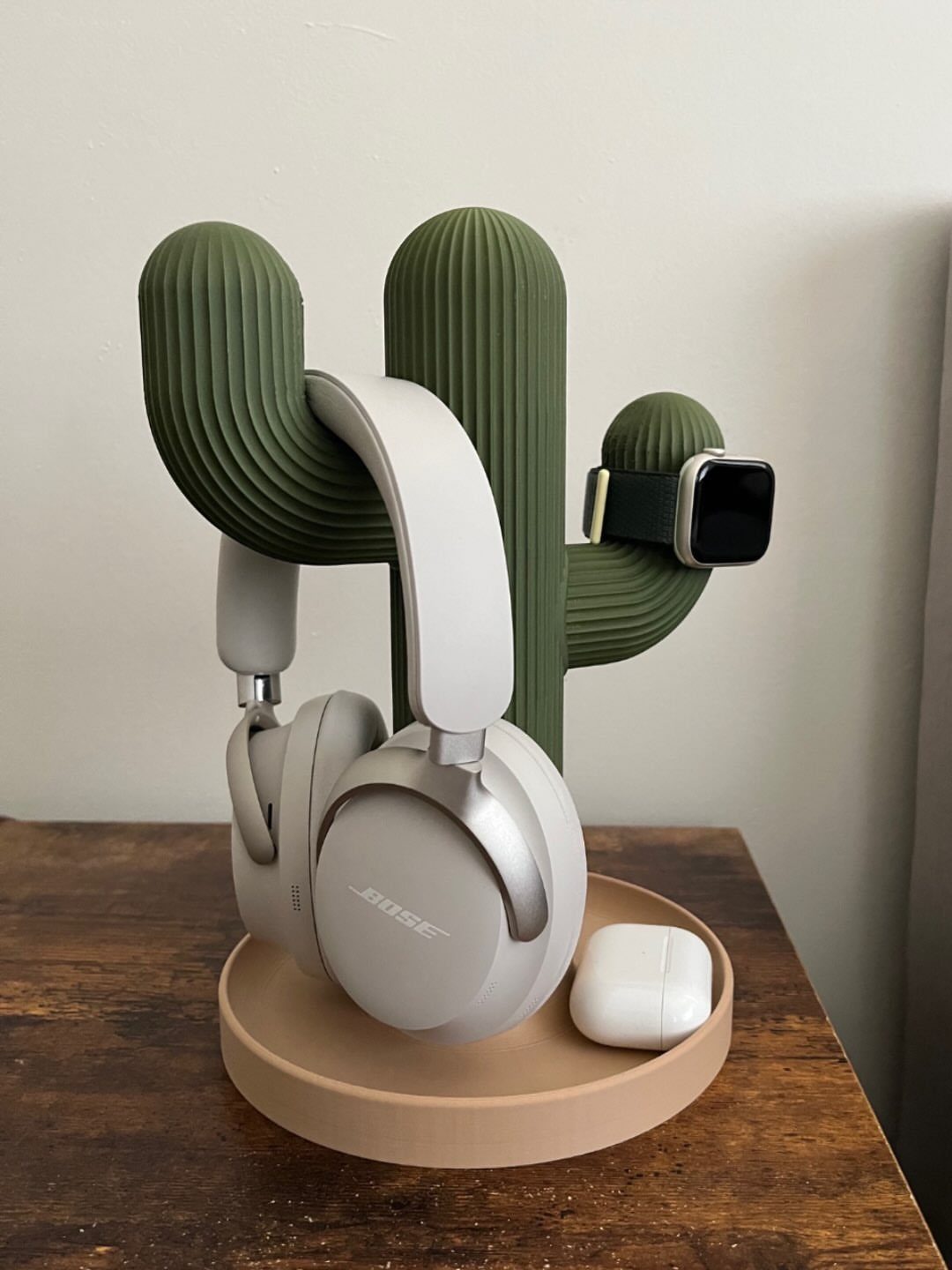 40 Home Decor Item Ideas, From Candle Holders to Sculptures 15 Cactus-shaped headphone organizer holding white headphones, a smartwatch, and earbud cases on wood.