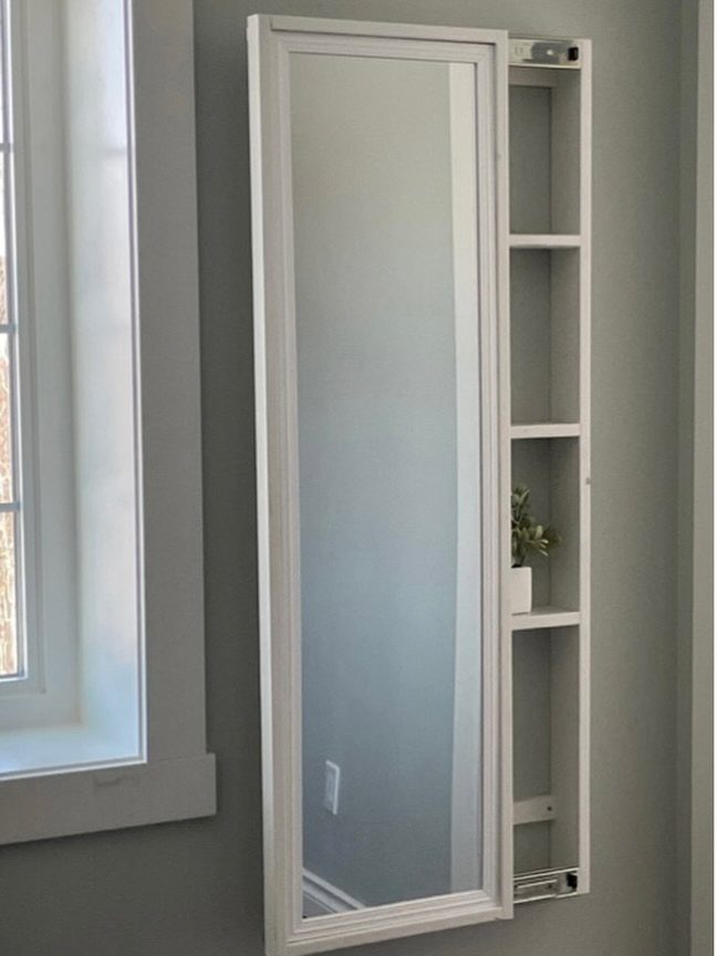 12 Small Bedroom Mirror Ideas That Make a Room Feel Bigger 3 White framed wall mirror with hidden storage shelves and a small plant.