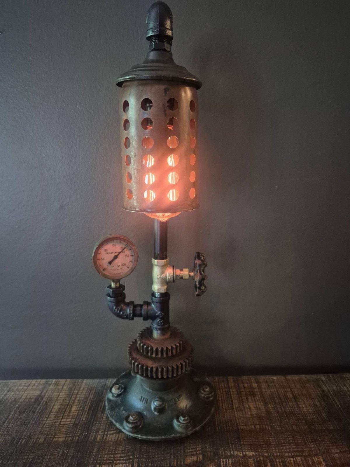 17 Handmade Lamps Ideas Using Wood, Concrete, and Glass Jars 2 Industrial metal pipe lamp with a pressure gauge and glowing perforated cylinder shade.