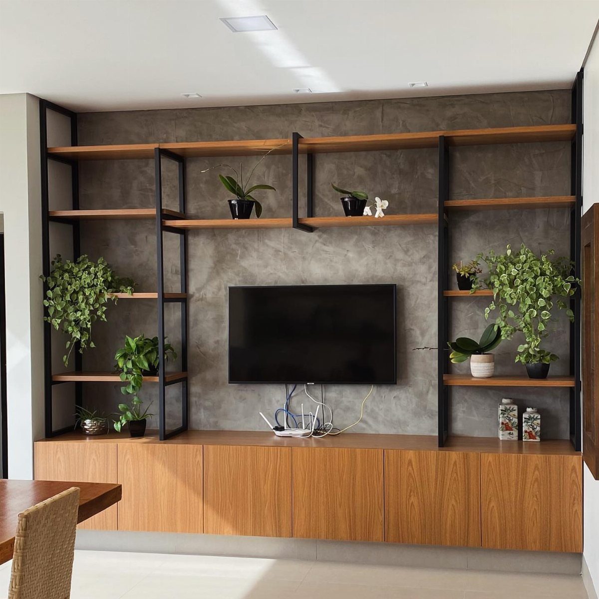 Modern industrial TV unit with wooden cabinets, black metal shelves, and concrete wall.