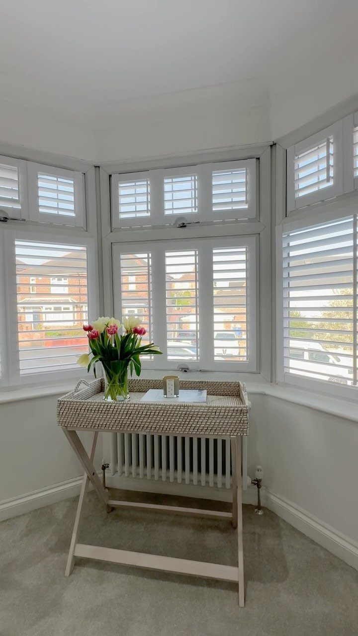 White interior shutters on a bay window with a flower vase on a table