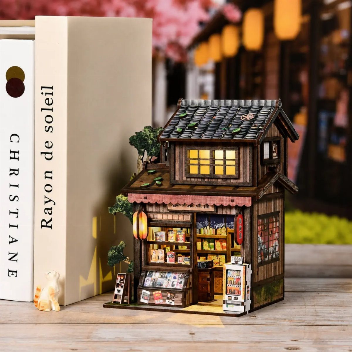 Miniature Japanese shop diorama with glowing lanterns placed next to a white book.