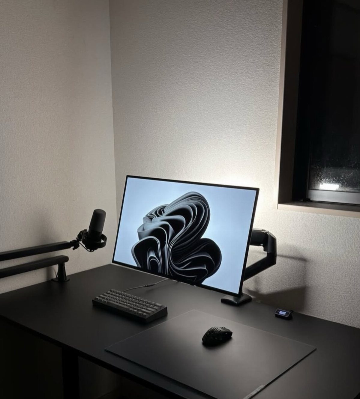 Minimalist black desk setup with monitor, keyboard, mouse, and microphone on a clean surface.