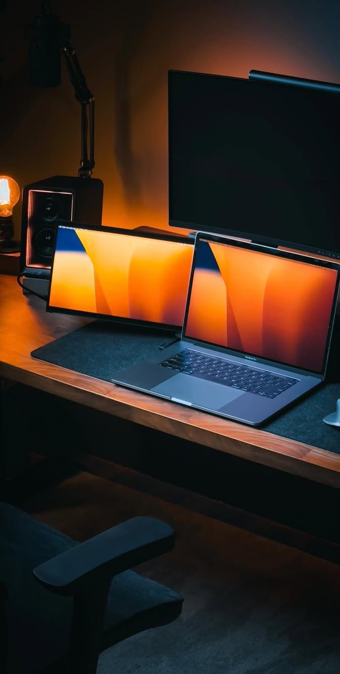 13 Double Monitor Desk Setup Aesthetic Ideas That Work 6 Laptop and monitor hybrid setup on a dark wooden desk with warm ambient lighting.