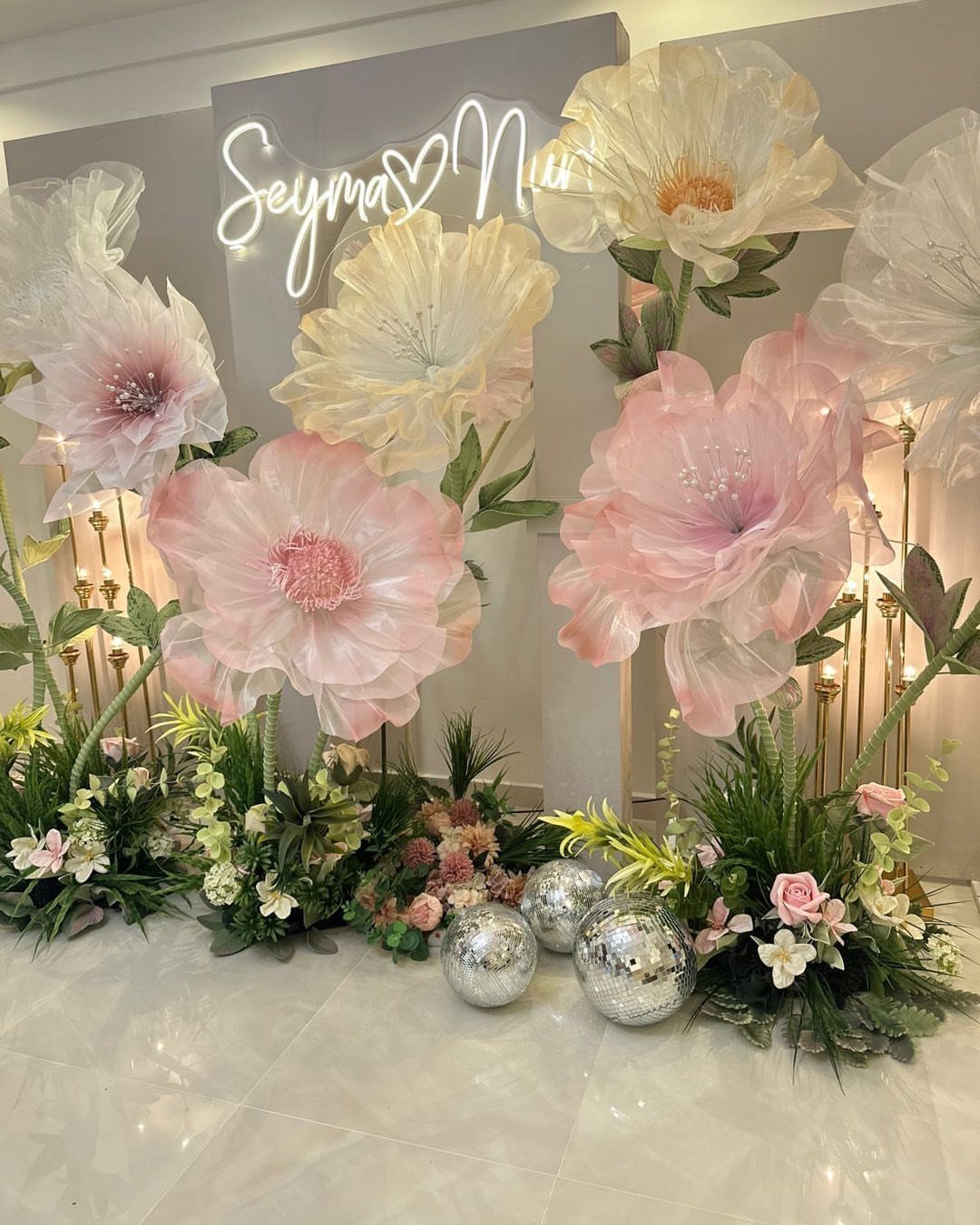 Large decorative paper flowers in pink and white with a neon sign and disco balls.