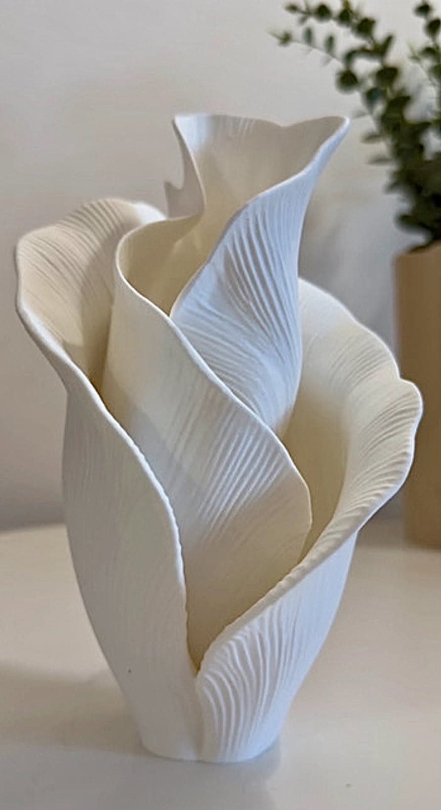 White ceramic vase shaped like a leaf with organic ridges on a white surface.