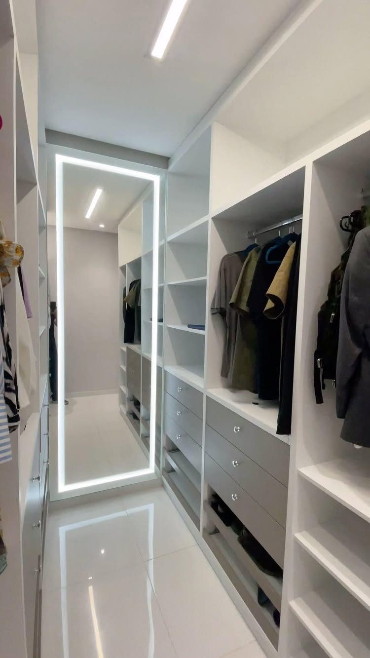 Full-length LED backlit mirror in a modern white walk-in closet with built-in shelving.