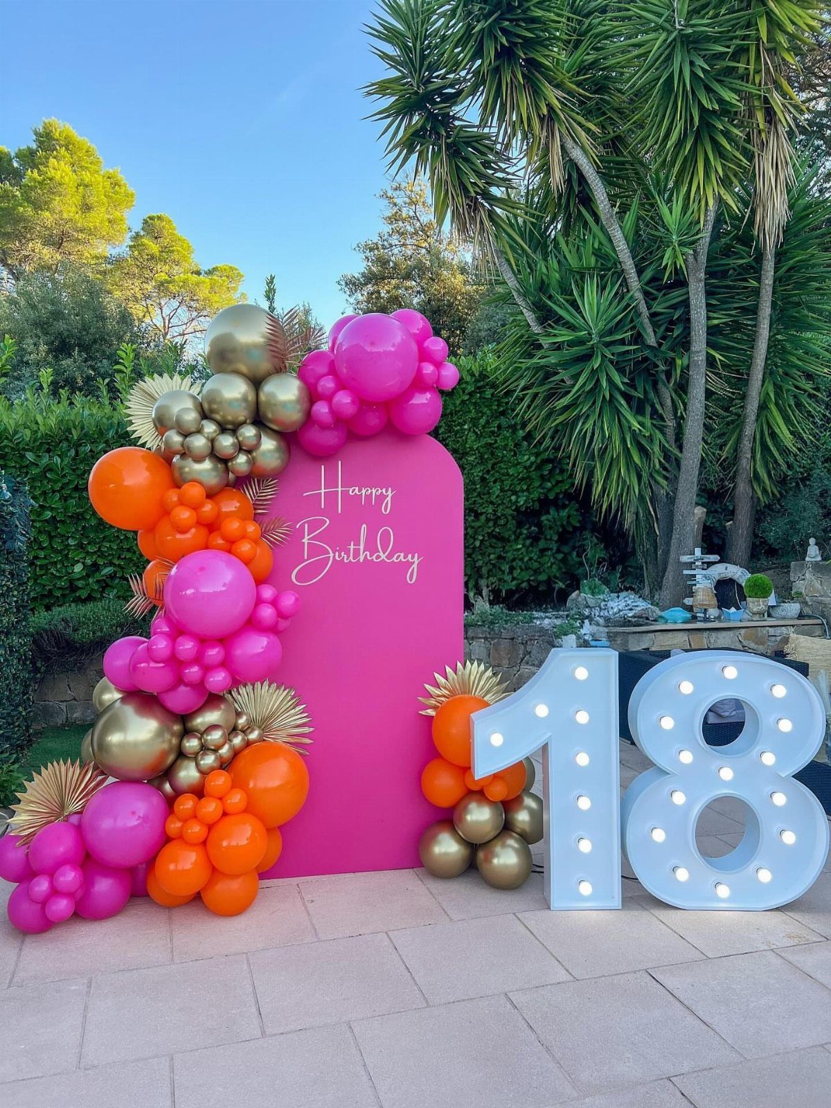 Pink birthday backdrop with gold and pink balloon garland and large glowing number 18.